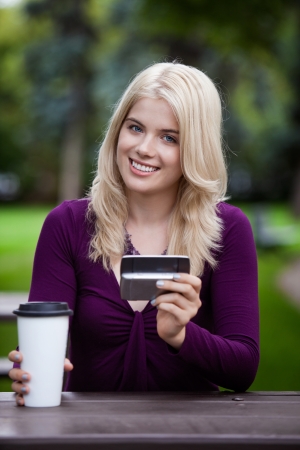 portrait of a happy smiling college student sitting in park with cell phone and coffee