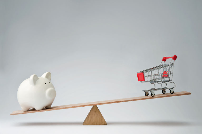 shopping trolley and piggy bank balancing on a seesaw